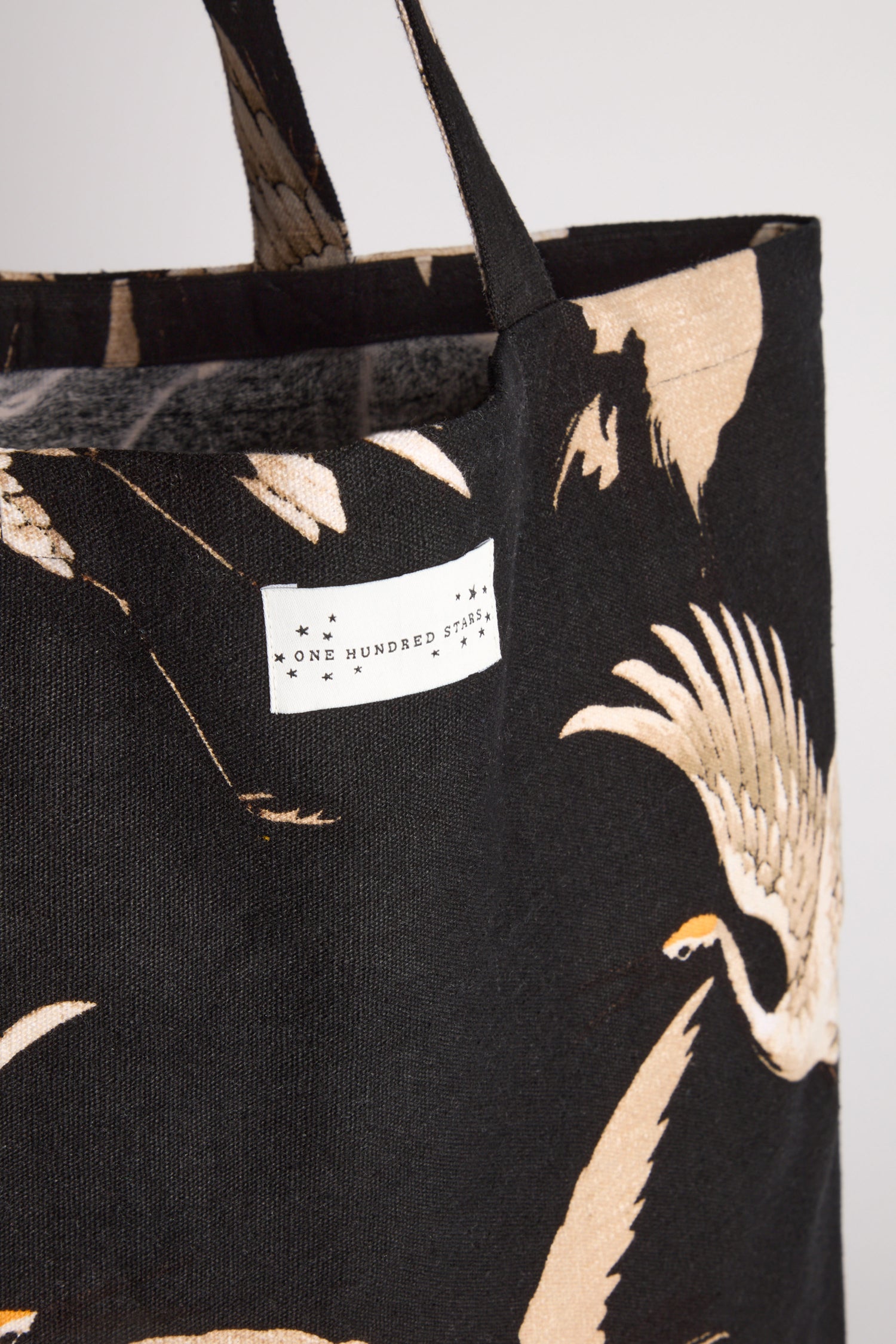 Close-up of the Stork Canvas Bag, made from sustainable cotton and featuring a beige bird print. The tag says "One Hundred Stars," representing its eco-friendly design.