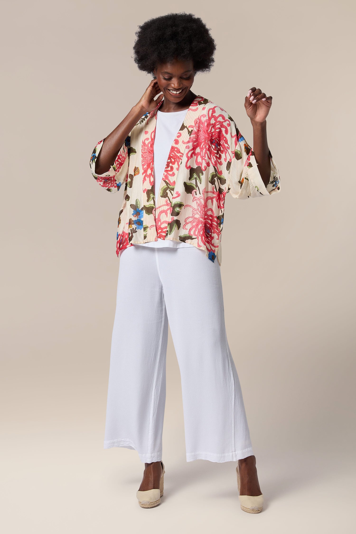 A black woman wearing white wide leg pants and an open front Chrysanthemum Kimono.