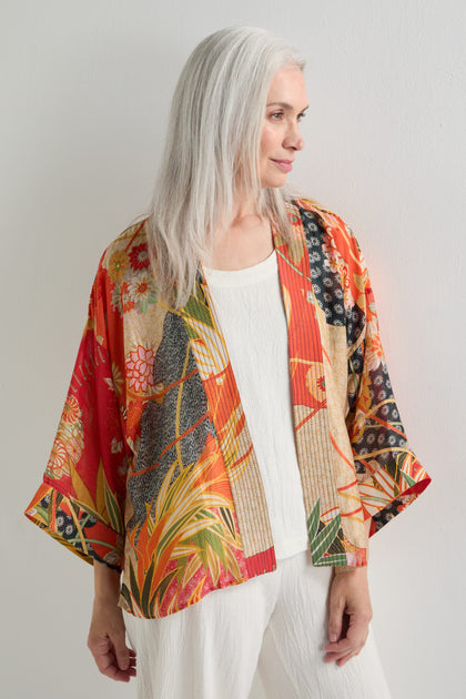 A woman with long gray hair models the Fans Print Kimono over a white top and pants, standing in front of a plain white wall.