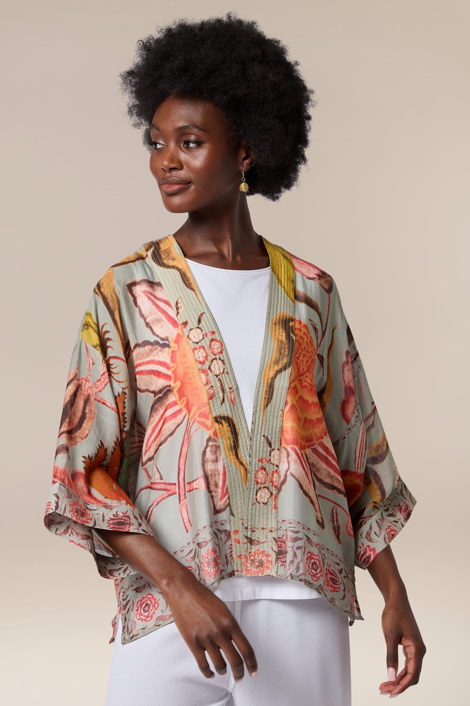 A black woman wearing a lightweight floral print Joy Kimono and white pants.