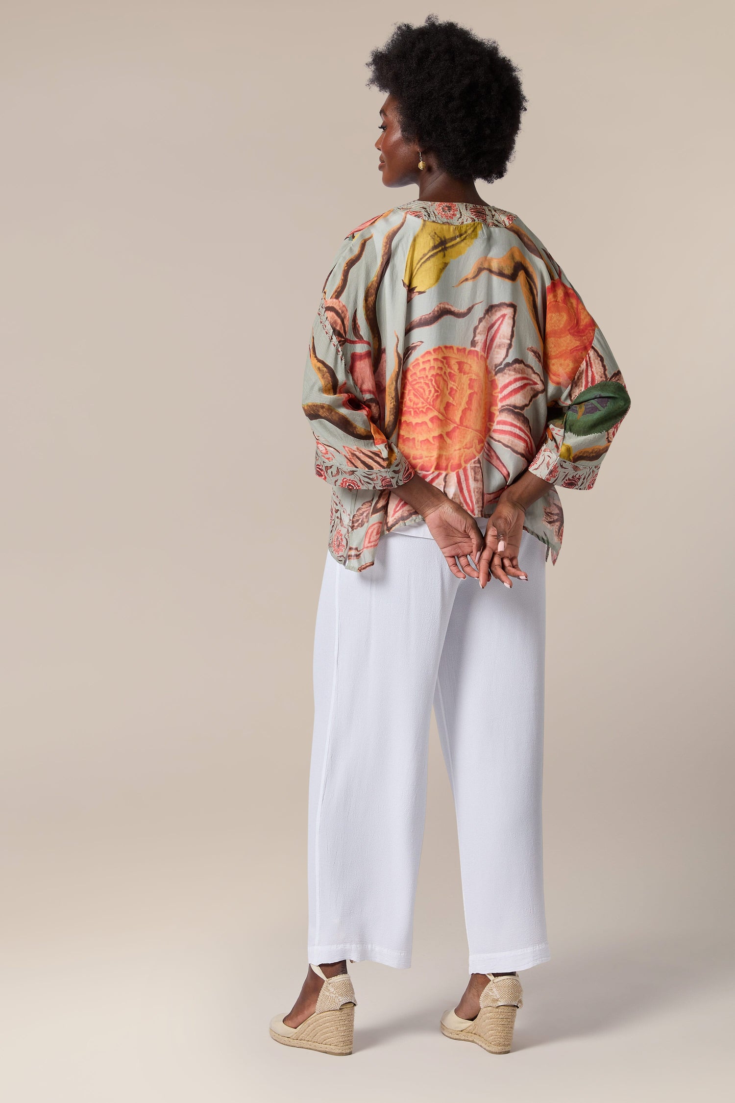 The back view of a woman wearing lightweight white pants and a printed blouse from Joy Kimono.