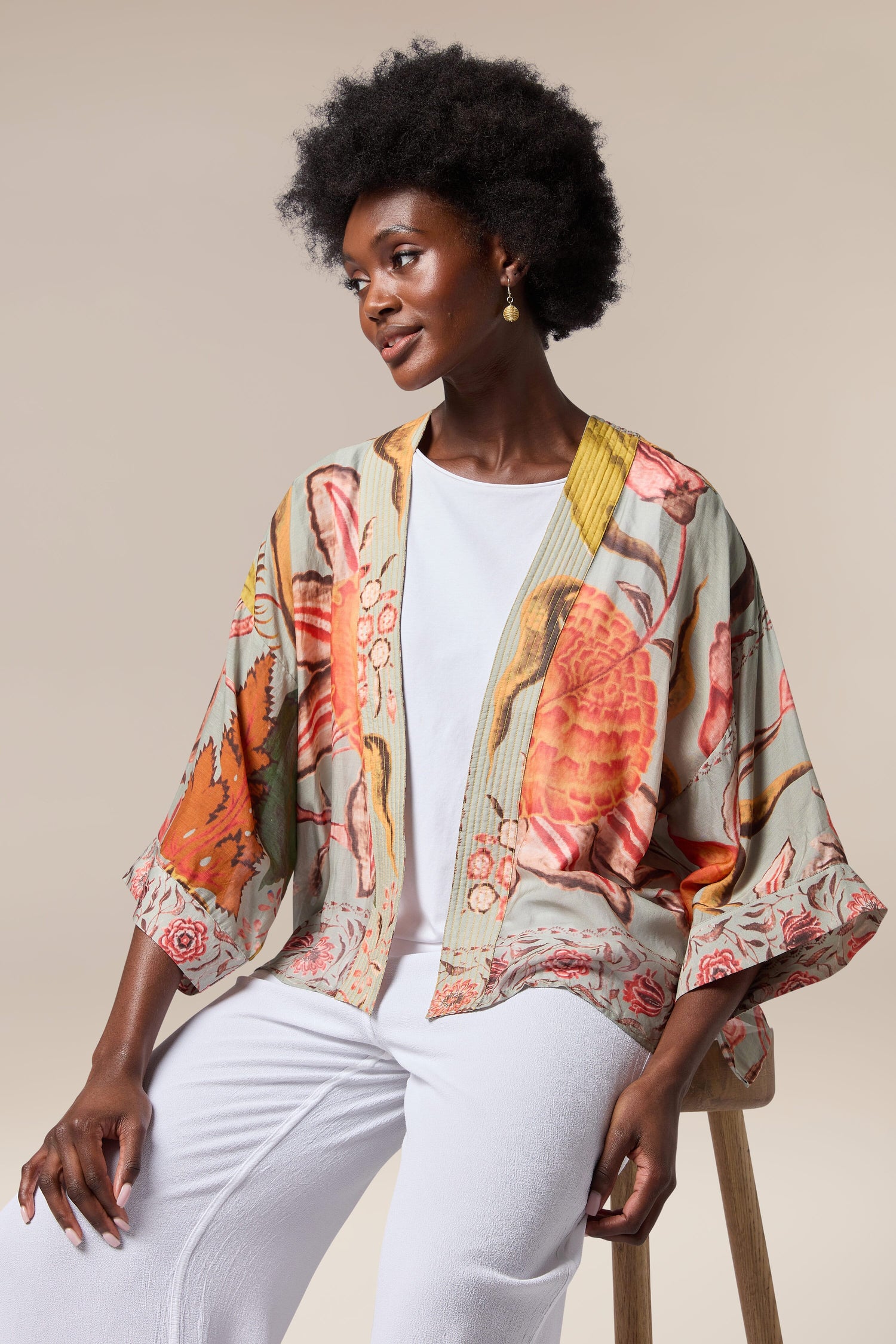 A woman is sitting on a stool wearing a lightweight, floral print Joy Kimono by One Hundred Stars.