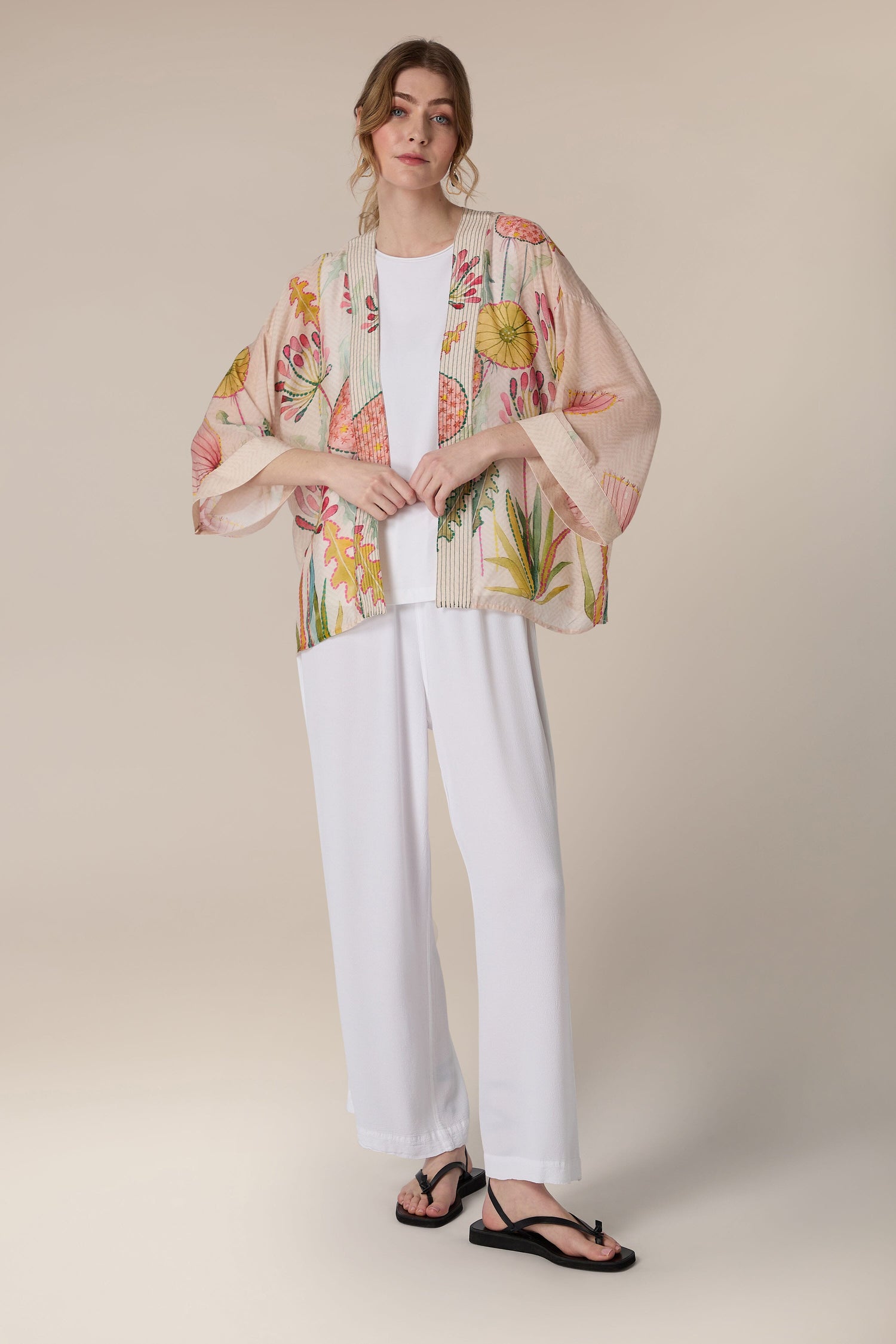 Woman modeling a Pop Flowers Kimono with white pants and sandals against a neutral background.