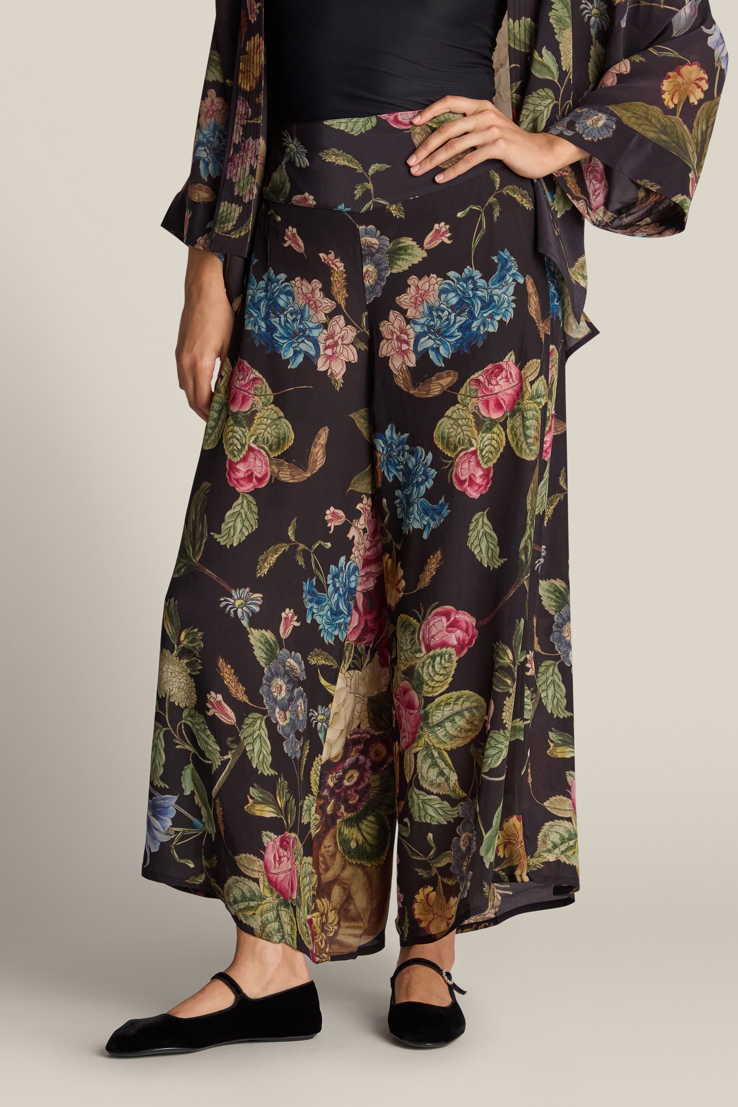 A person wearing Primula Palazzo Trousers with a painted floral print and black shoes, accentuated by a matching floral fabric draped over one shoulder.