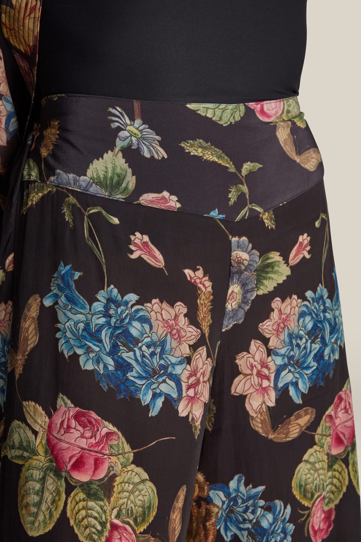 Close-up of a person's midsection wearing a black Primula Palazzo Trouser featuring colorful flower designs, including blue, pink, and rose painted floral print.