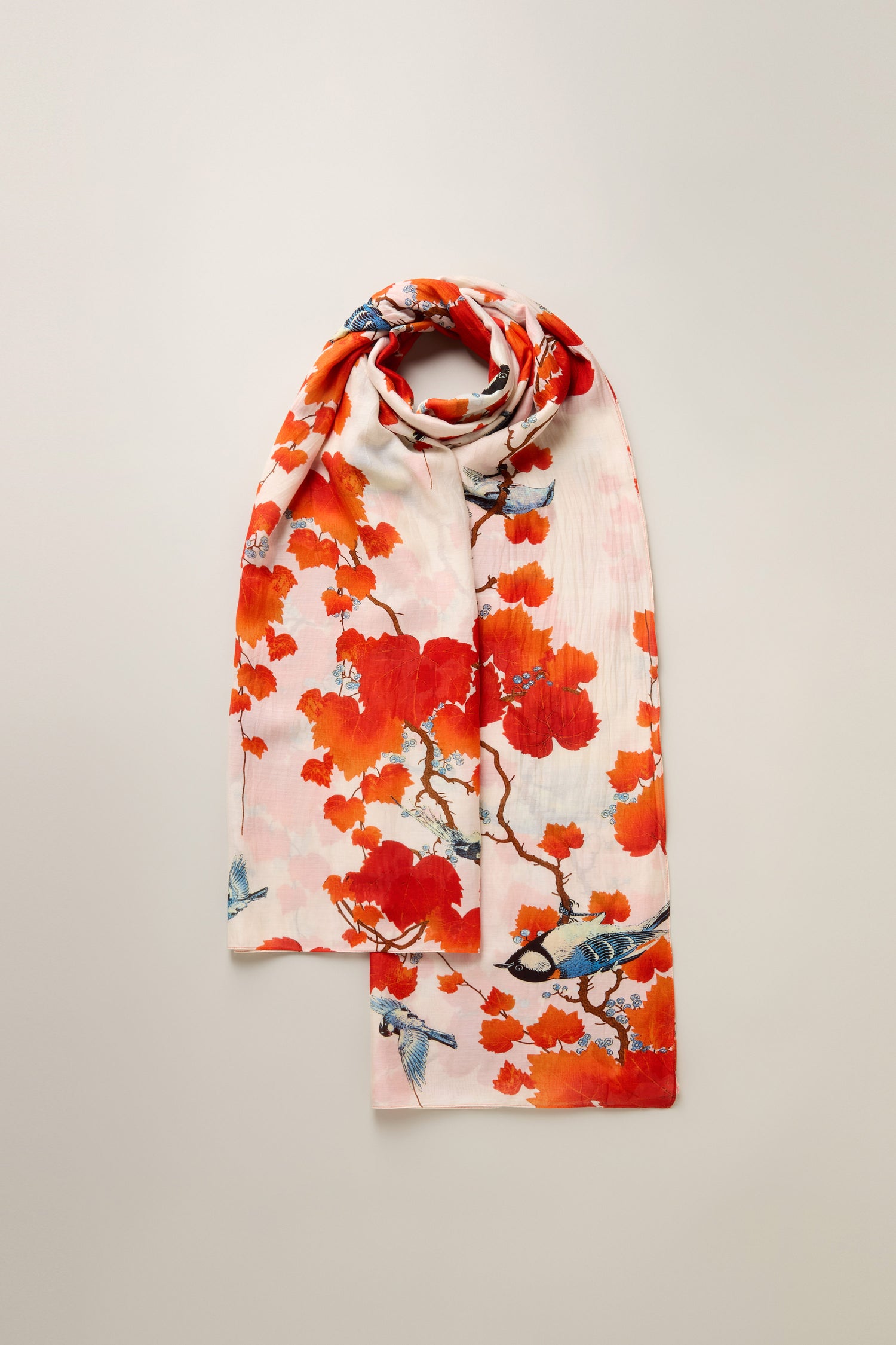 The Acer Print Scarf is a folded pink scarf adorned with vibrant orange floral and bird patterns on a light background, crafted from a silky modal-cupro blend.