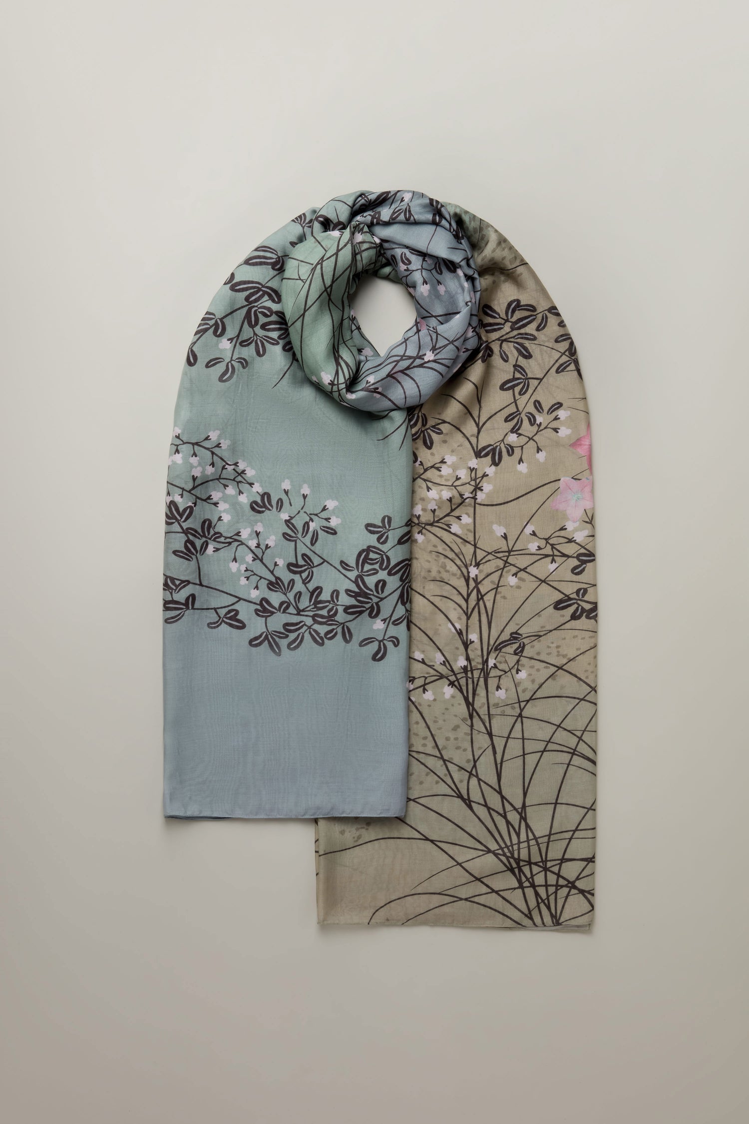 A Dunes Print Scarf, showcasing an intricate hand-drawn botanical pattern in green and beige, is elegantly looped on a plain background.