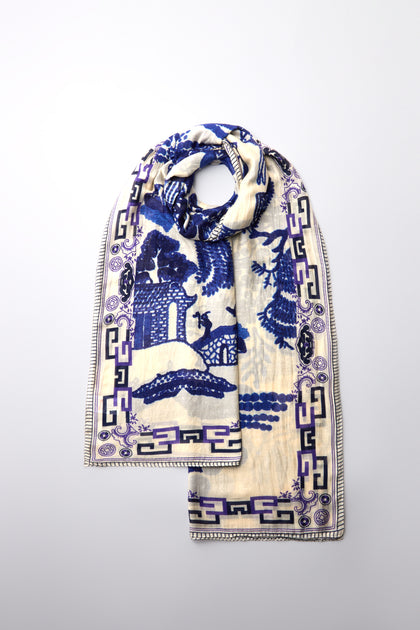 The Willow Print Scarf in white, featuring blue and purple abstract and geometric patterns, exudes timeless elegance on a simple gray background.