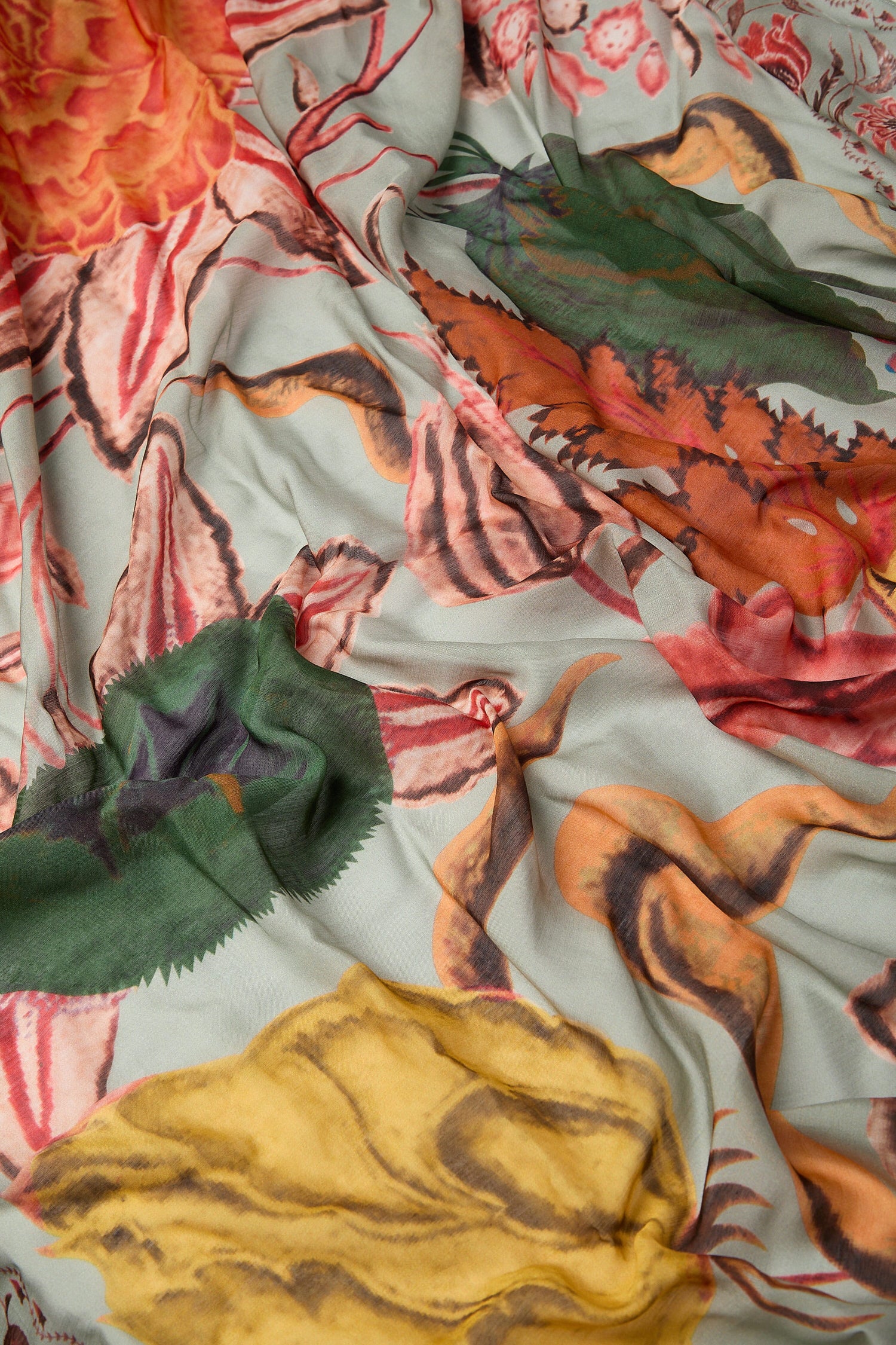 Sentence with product name: The Joy Scarf, with its vibrantly patterned hand-painted design in a mix of warm and cool tones, drapes elegantly to showcase its beauty.