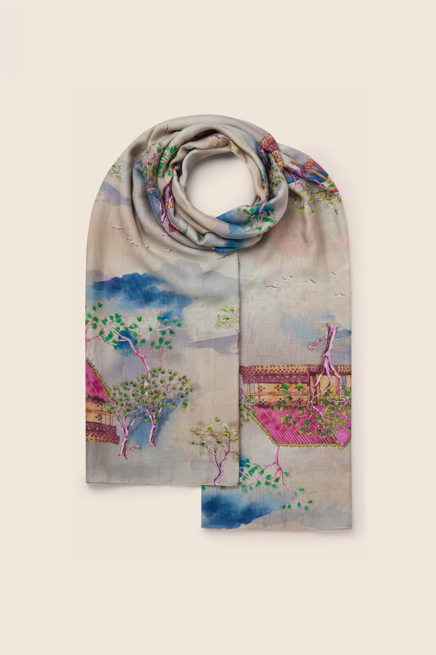 The Landscape Scarf is a light-colored accessory made from silky viscose, featuring a printed design of trees, rooftops, and birds in pastel tones that evoke Japanese landscape watercolors. This scarf perfectly embodies nature-inspired prints.