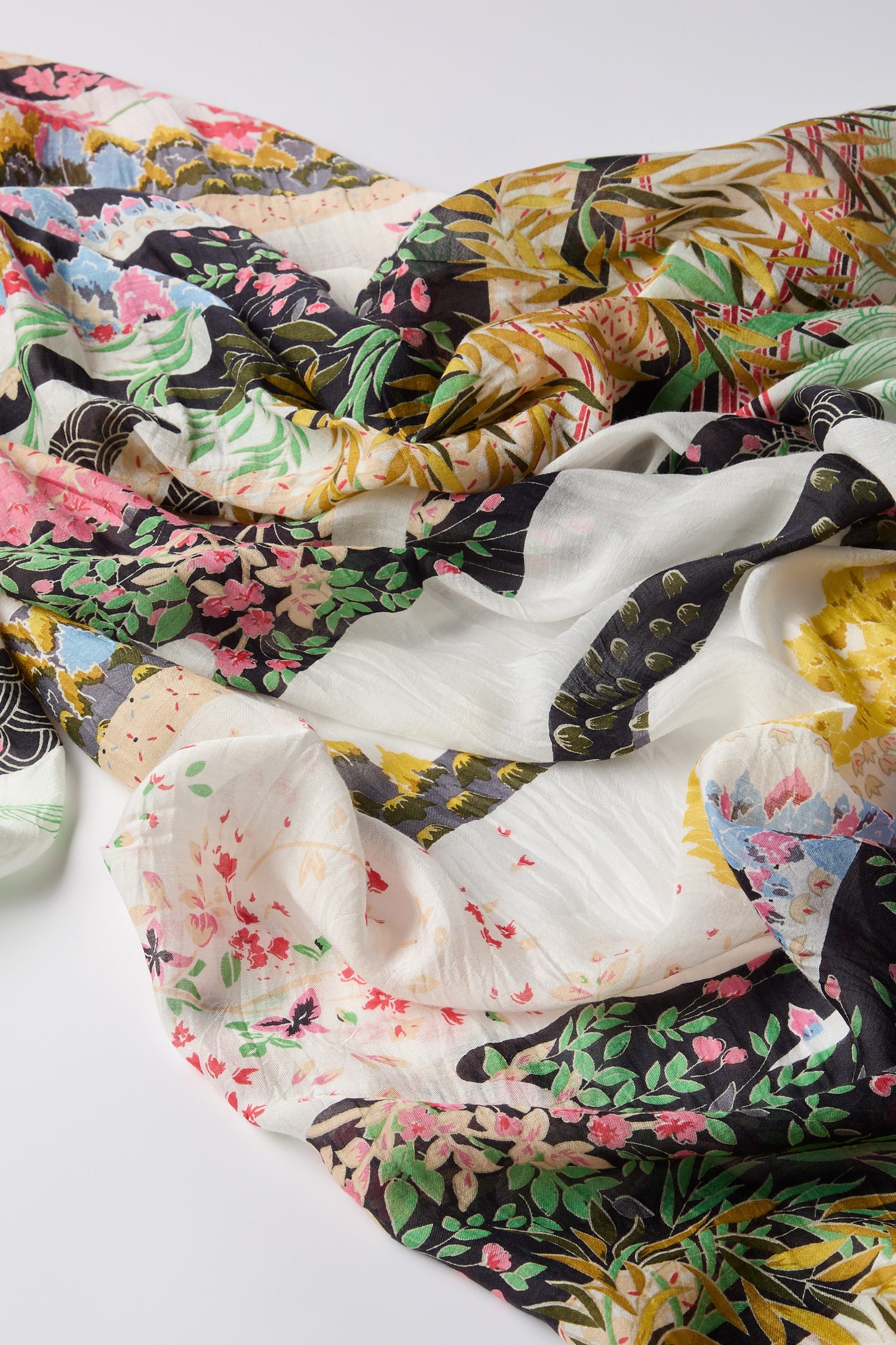 The Spring Print Scarf features a vibrant floral pattern inspired by an oriental garden, showcasing a mix of flowers, leaves, and abstract designs on a light background.