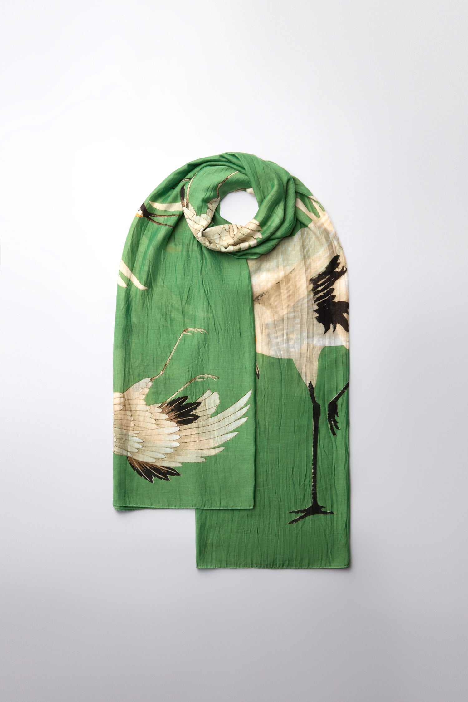 The Stork Print Scarf is an Art Deco-inspired green accessory featuring bold crane birds in black and beige, elegantly soaring on a plain white backdrop, creating a remarkable statement piece.