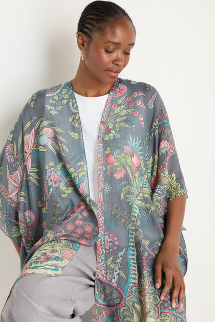 A woman wearing the Boho Garden Print Throwover over a white top and light gray pants looks down with a neutral expression.