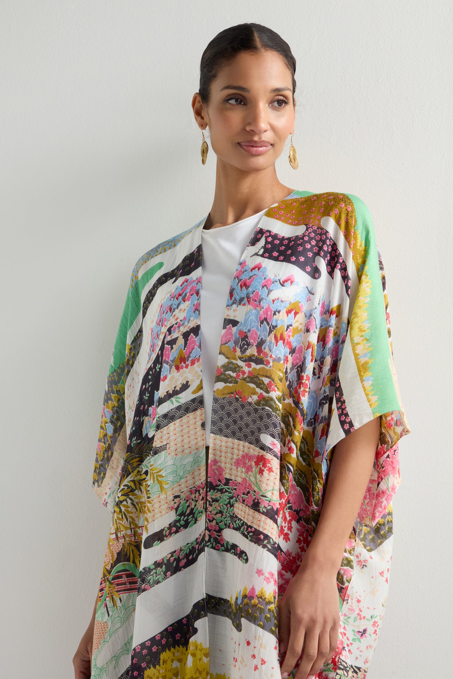 A person wearing a Spring Print Throwover, featuring colorful patterns reminiscent of Japanese landscapes, over a white top, stands against a neutral background.