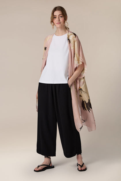 Sentence with Product Name: A woman stands posing in a casual outfit comprising a white t-shirt, black wide-leg pants, an Indian textiles patterned Angled Hem Throwover, and black sandals.