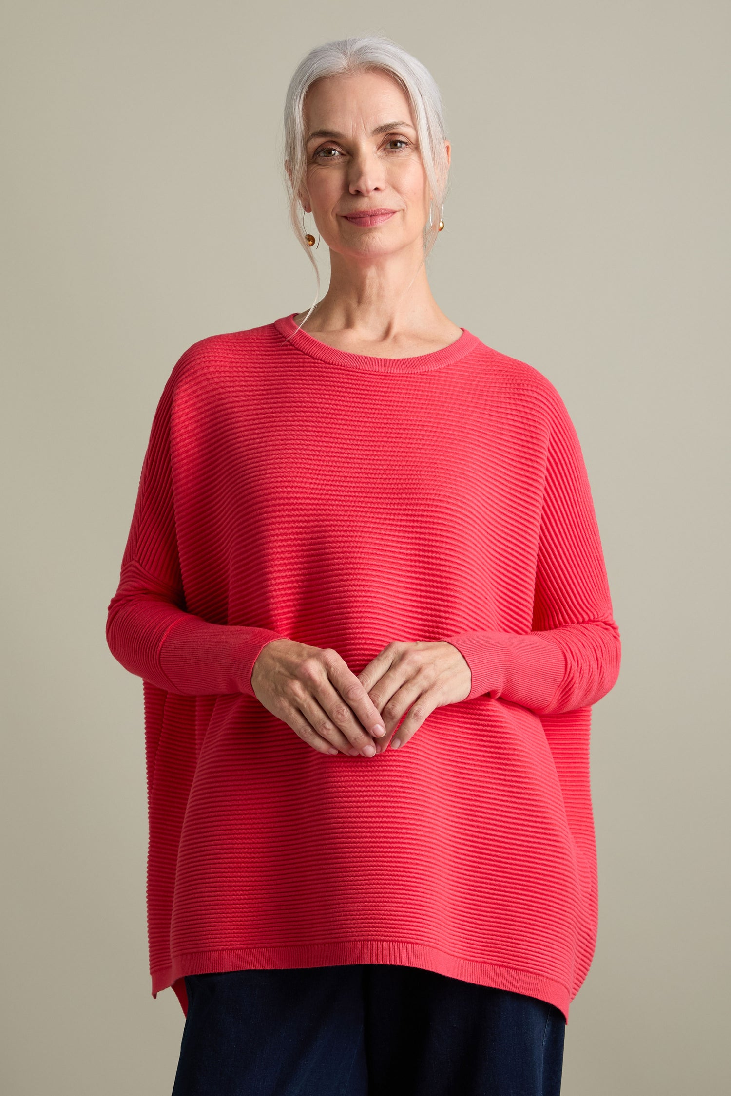 A woman with gray hair, wearing a bright red Ribbed Jumper that exudes a luxurious feel, stands against a plain background.