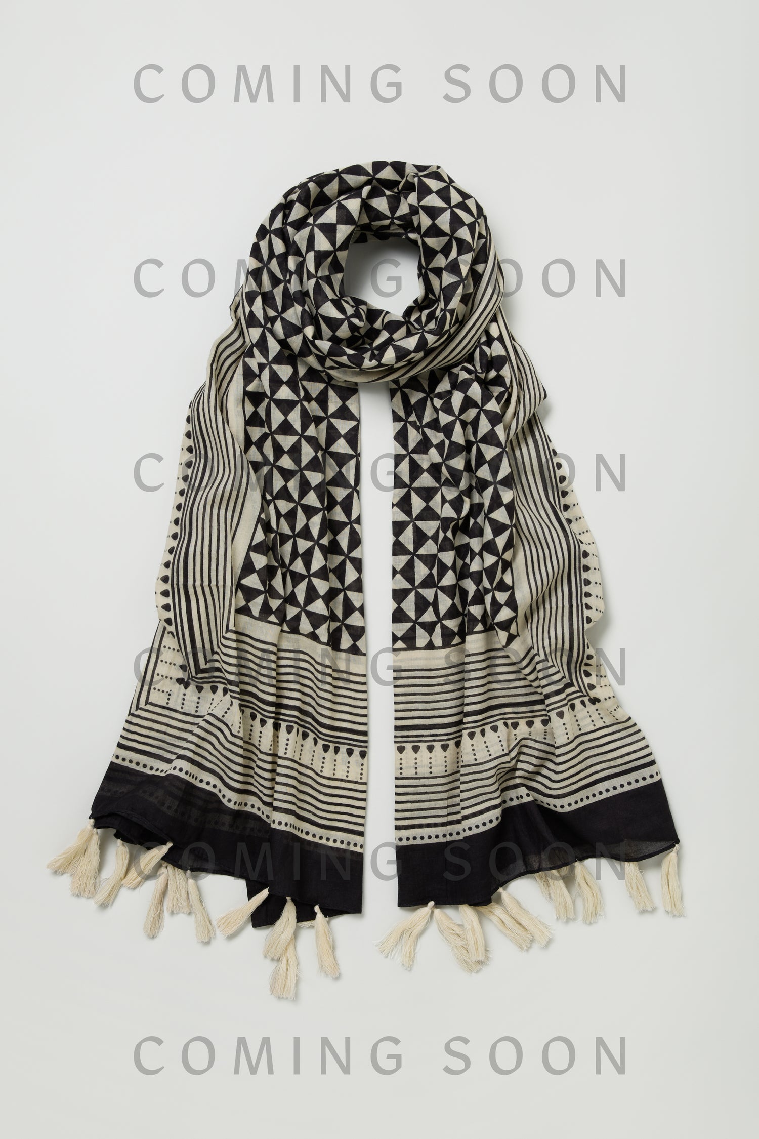 The Cotton Tassel Scarf, style PMC180072A, features black and white geometric patterns and tasseled edges. It's displayed on a light background with "COMING SOON" overlaid on the image.
