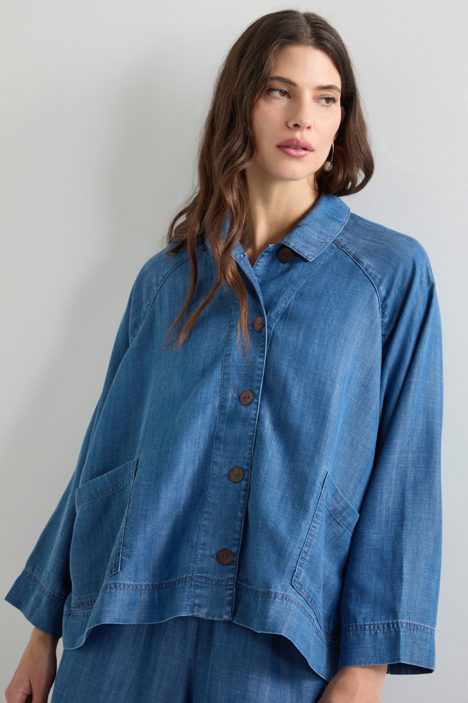 Wearing the Fluid Denim Boxy Jacket, a person stands against a neutral background, embodying the essence of fluid denim.