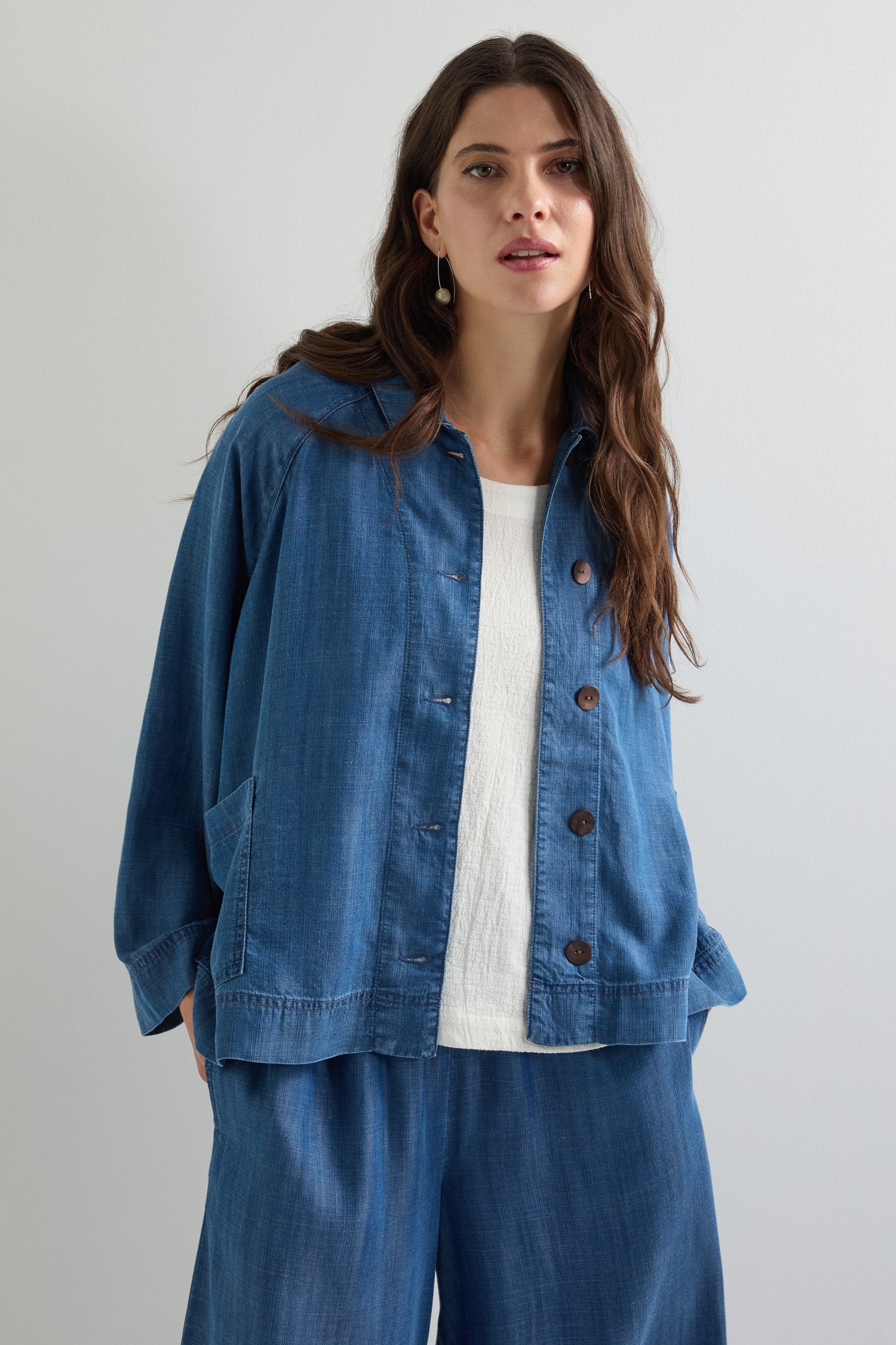 A woman is wearing a Fluid Denim Boxy Jacket over a white top and matching blue pants, standing against a plain background.