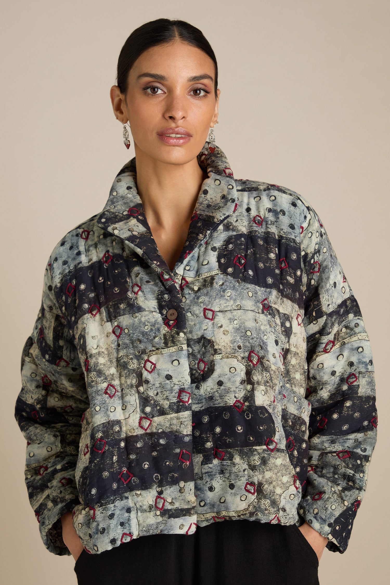 Person wearing a Padded Embroidered Cotton Jacket with a mix of dark and light patches, featuring red and white details, standing against a neutral background. The 100% cotton fabric boasts intricate embroidery, adding a touch of elegance to the striking design.