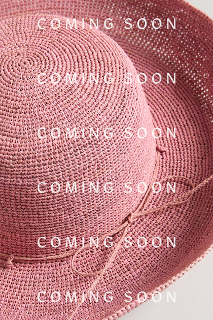 A Handwoven Wide Brim Raffia Hat in pink with a thin braided band, overlaid by repeated "COMING SOON" text and the RABB12 signature.
