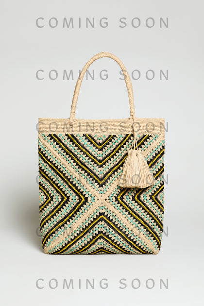 A Handwoven Raffia Tote Bag with black, beige, and green zigzag patterns, plus tassel and rope handle. The image displays "COMING SOON" text repeatedly.