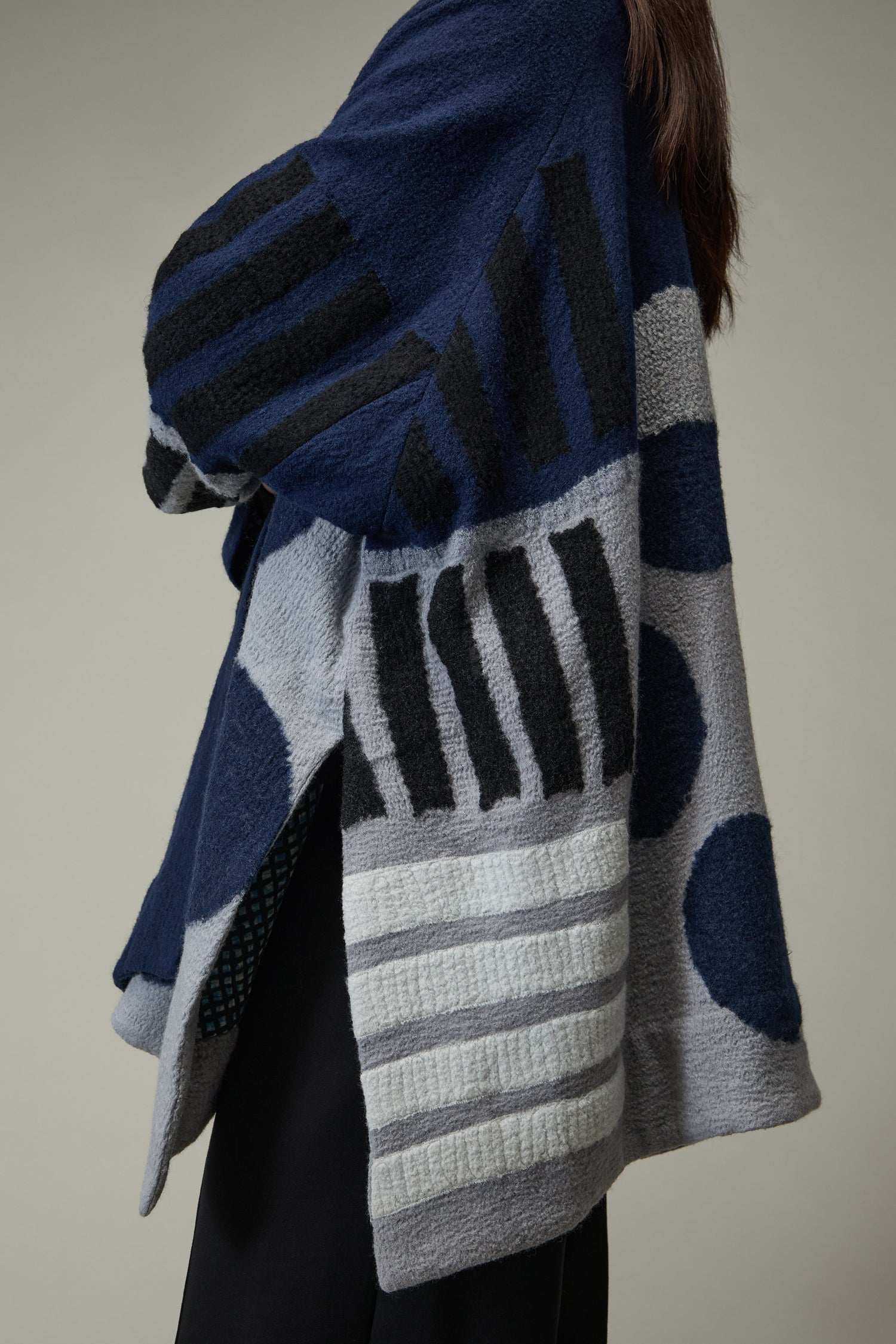 Model wears the Spot and Dash Wool Jacket, featuring blue, grey, and black color blocks with stripes and polka dots in an abstract pattern, shown from the side against a plain background.