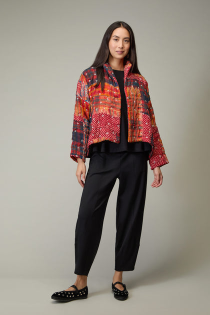 A woman stands against a plain background wearing the Padded Multi Check Padded Jacket, paired with black pants and black flats with white dots.