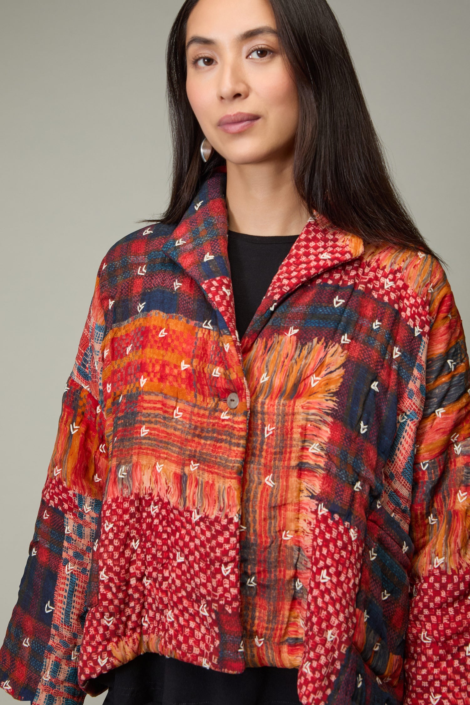 A woman with long dark hair models the Padded Multi Check Padded Jacket, which features a vibrant red, orange, and blue check pattern on a neutral background.