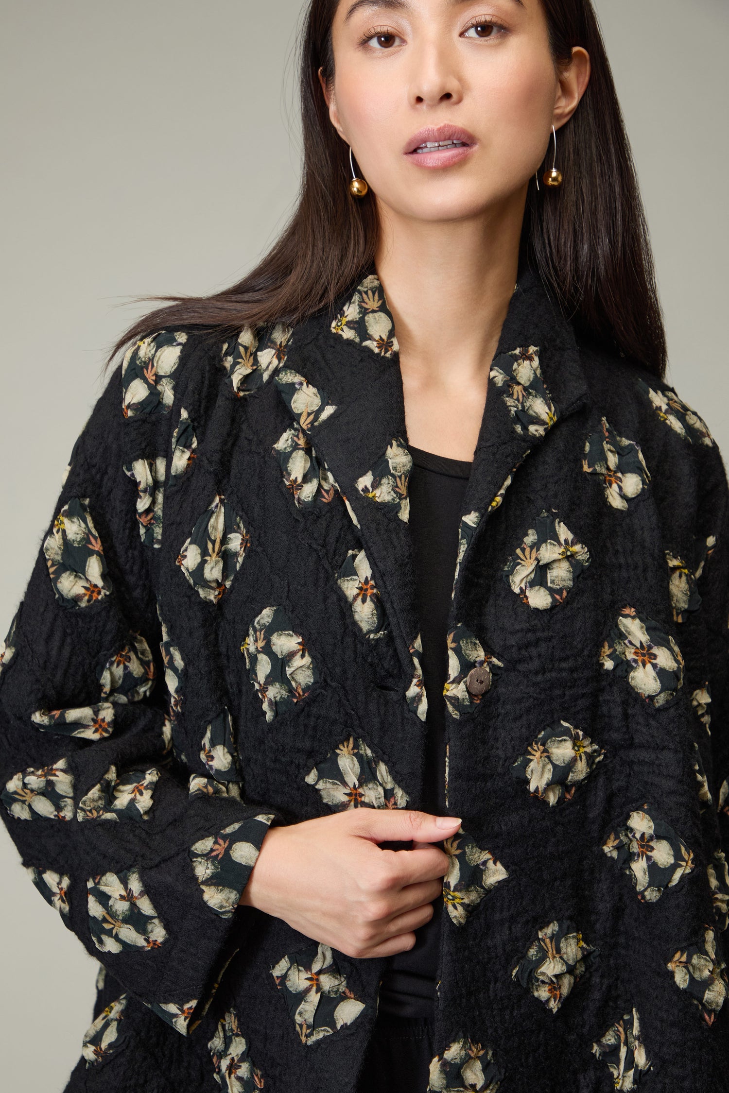 A woman wearing the Textured Flower Wool Jacket with a floral pattern and gold earrings stands against a neutral background.