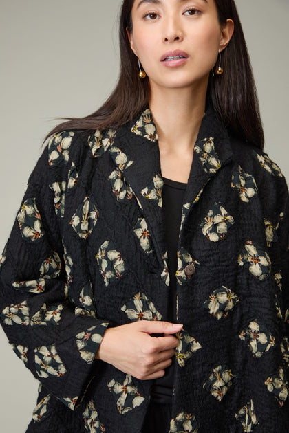 A woman wearing the Textured Flower Wool Jacket with a floral pattern and gold earrings stands against a neutral background.