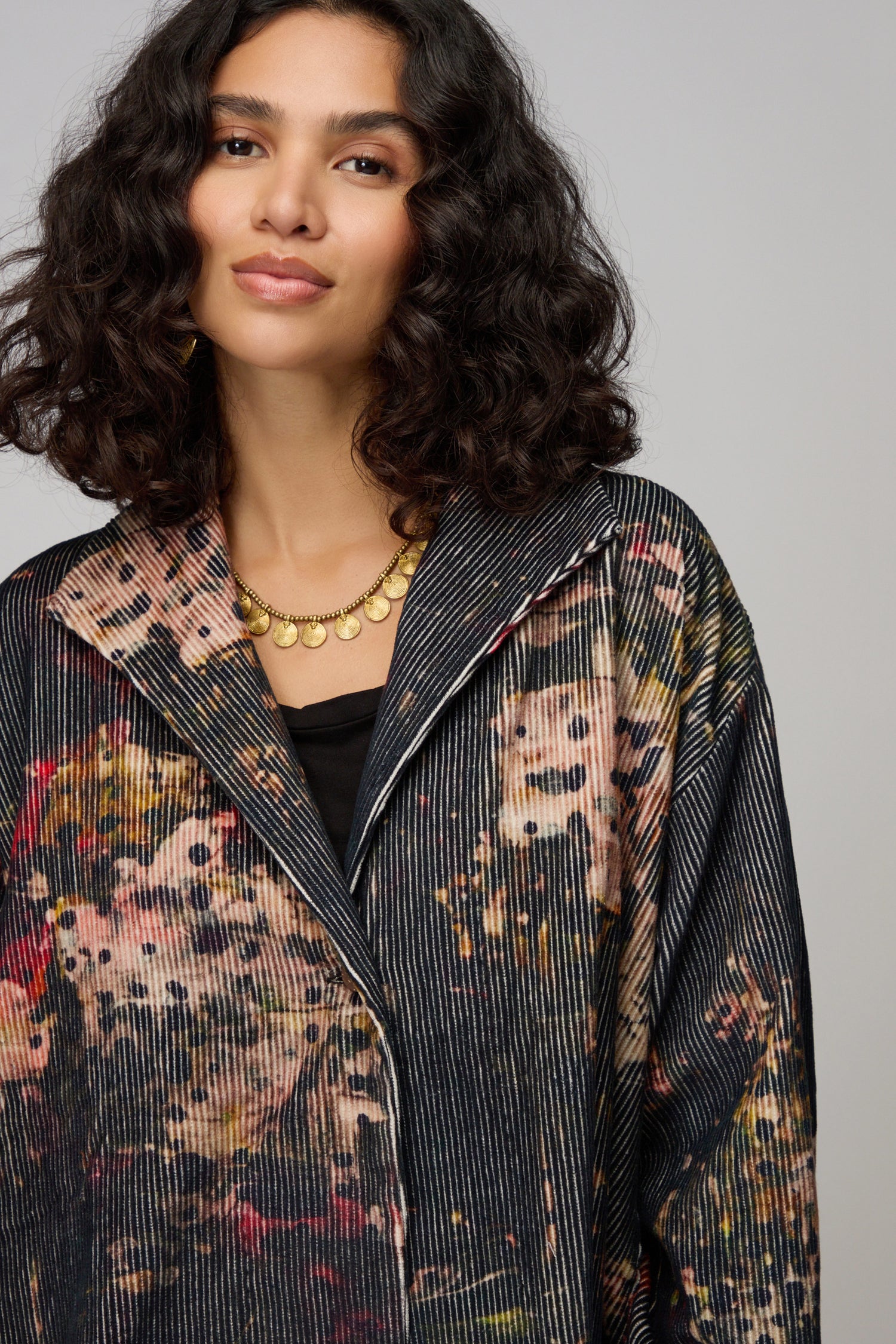 A woman wears the Print Corduroy Jacket with a relaxed fit over a black top and maroon pants, standing against a plain background.