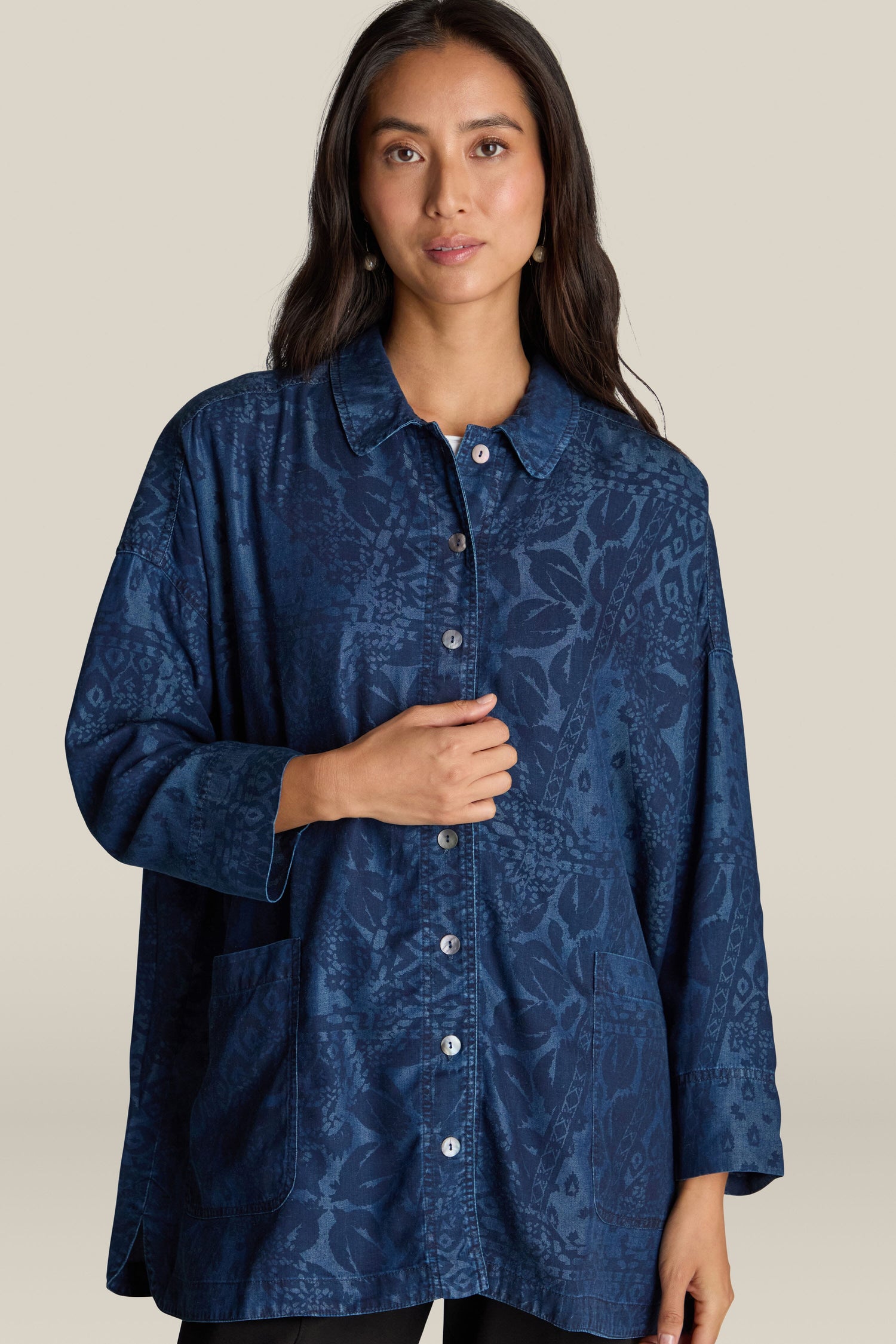 A woman with long dark hair wears an Abstract Patchwork Print Shirt, featuring a navy blue patterned design and button-down style with pockets, set against a plain background for a contemporary edge.