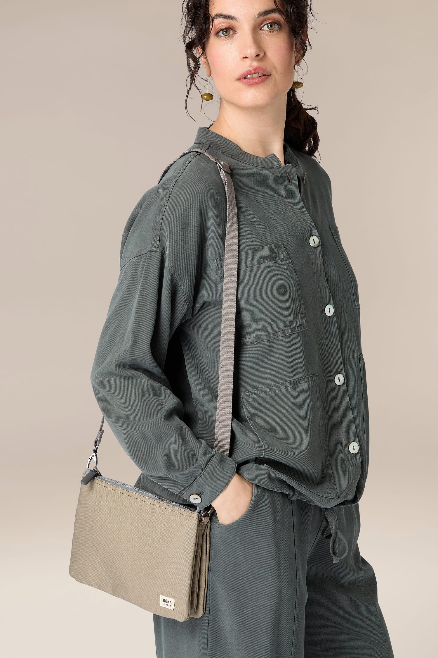 A woman carrying a Angela Roi Recycled Carnaby Crossbody Bag and wearing khaki pants.