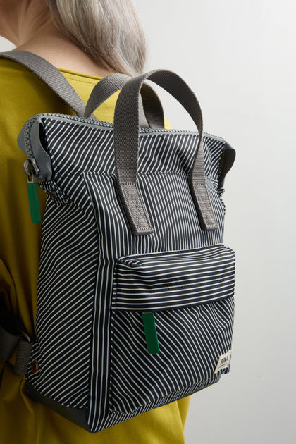 A person in a yellow top carries the Recycled Canvas Stripe Bantry Bag, a versatile backpack made from recycled canvas with gray straps, a front pocket, and a chic black-and-white striped design.