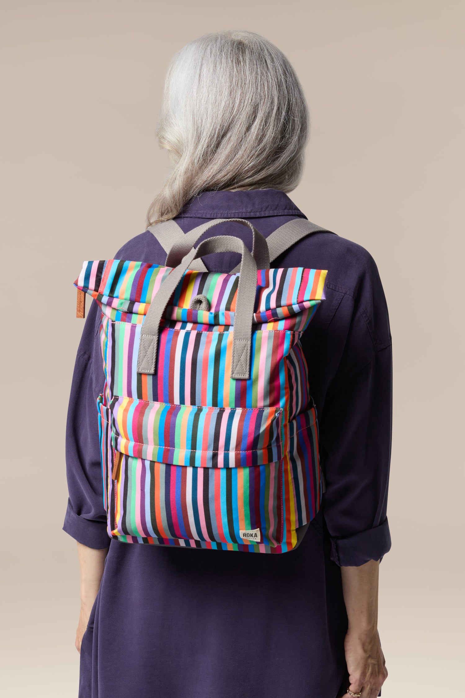 The back of an older woman wearing a Recycled Canvas Canfield Bag, a colorful striped roll-top design that is weather-resistant.