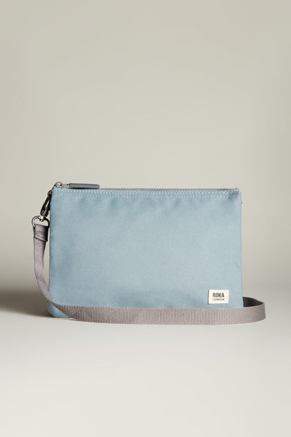 A light blue, weather-resistant rectangular Recycled Canvas Carnaby Crossbody Bag with a gray strap, featuring a small white label on the front.