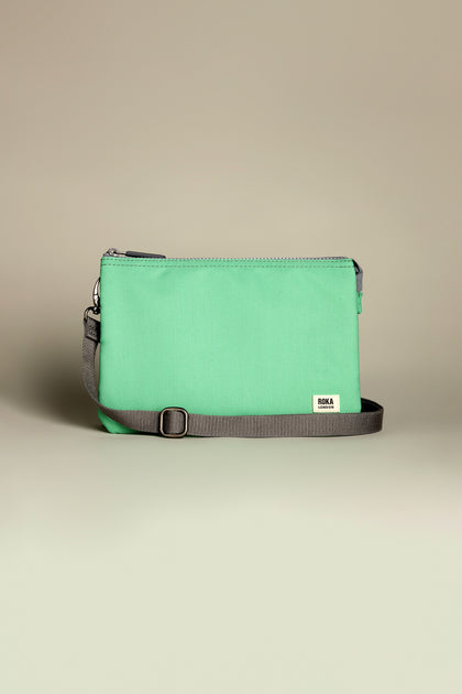 The Recycled Canvas Carnaby Crossbody Bag features a rectangular mint green pouch with a gray adjustable strap and zipper, all made from recycled canvas against a neutral backdrop.