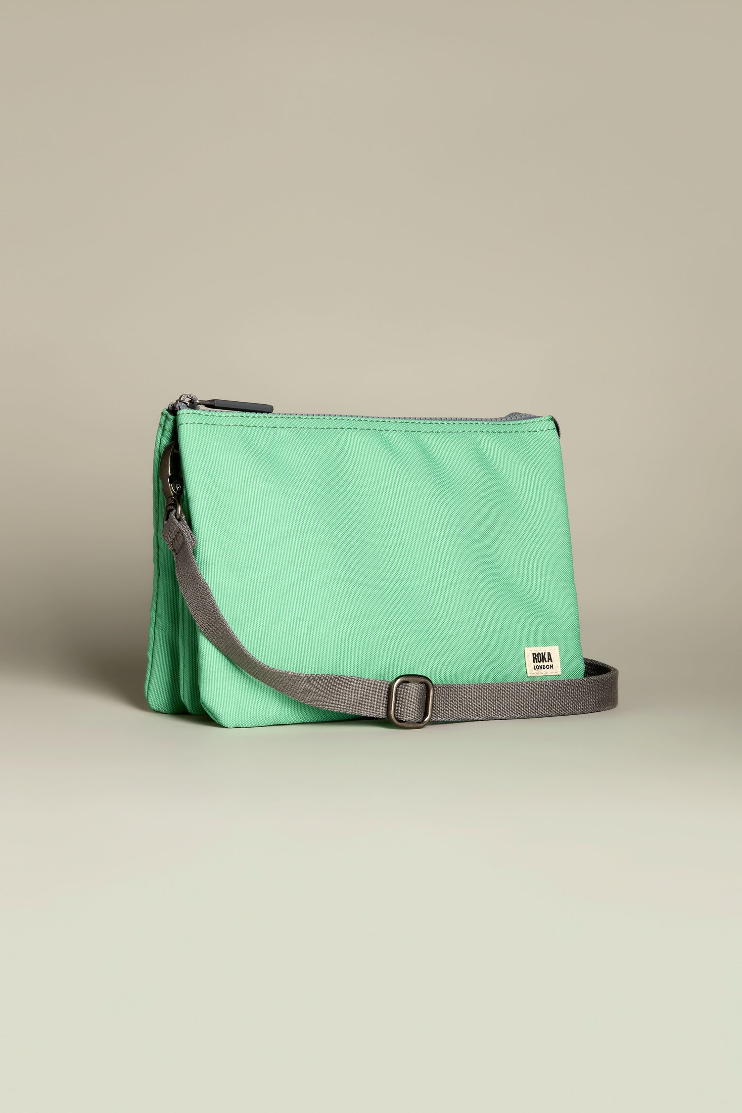 The Recycled Canvas Carnaby Crossbody Bag is a small, green gem with a gray adjustable strap and subtle side brand tag, elegantly displayed against a plain backdrop.