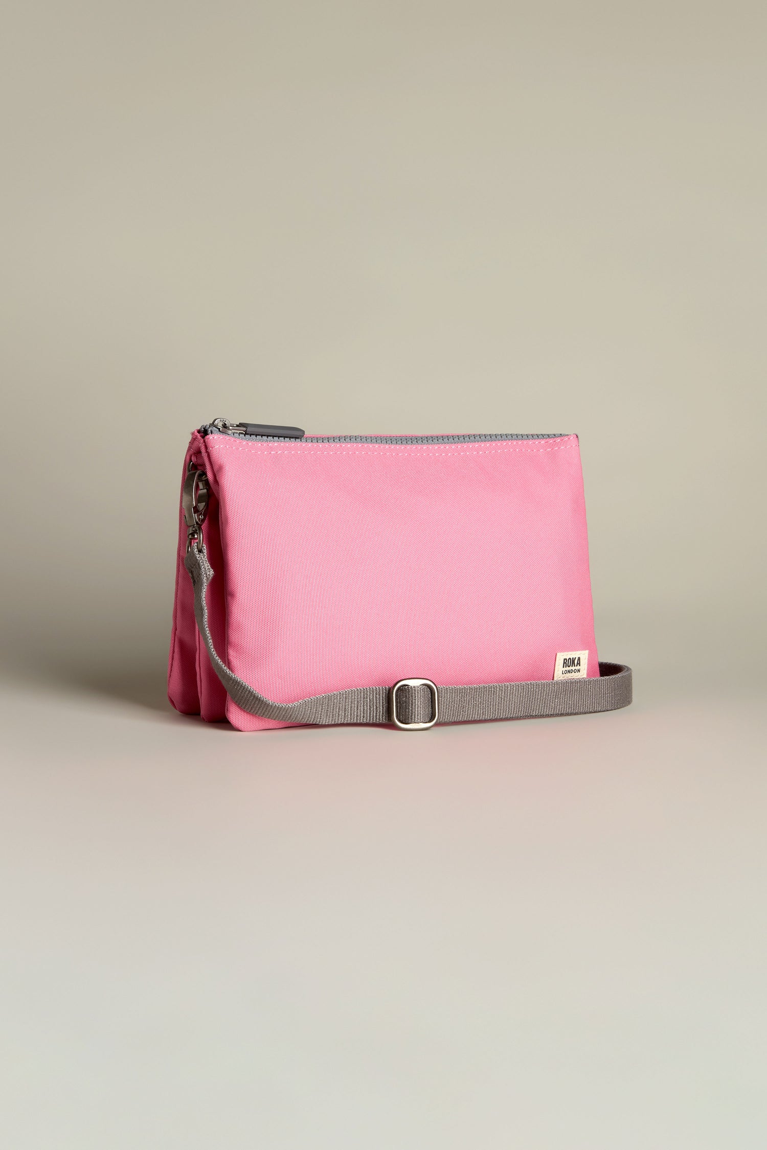 The Recycled Canvas Carnaby Crossbody Bag in pink features a gray adjustable strap and zipper, with "IRMA" on the front, set against a neutral background.