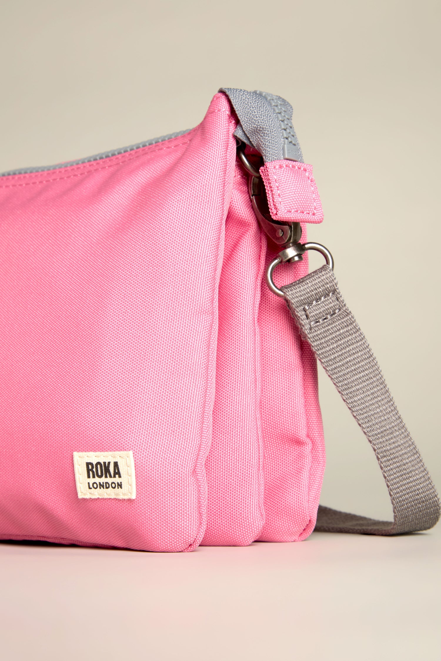 Recycled Canvas Carnaby Crossbody Bag in pink with an adjustable gray strap and "ROKA LONDON" label on the front.