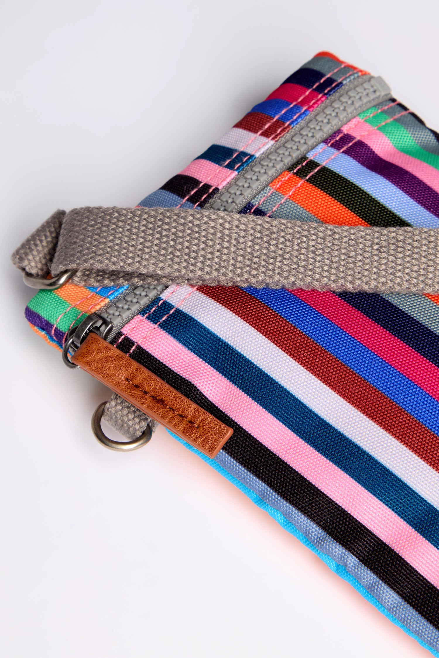 Discover the Recycled Chelsea Crossbody Bag: a close-up look at its multicolored striped fabric, crafted from recycled materials. It features a gray strap and small metal ring attachment, offering both style and weather-resistance for your daily adventures.