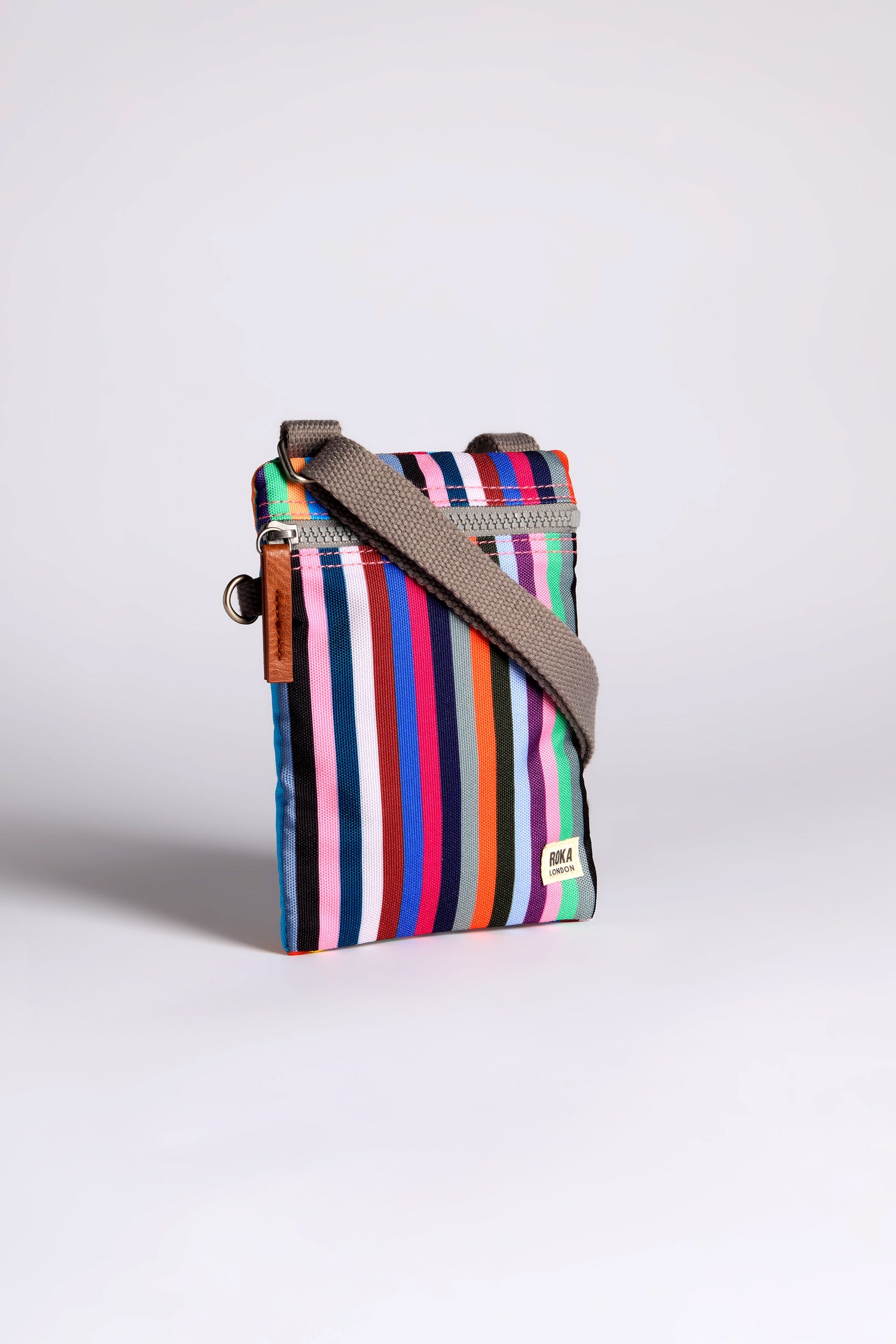 The Recycled Chelsea Crossbody Bag is a vibrant striped shoulder bag, crafted from recycled materials with a sleek gray strap, showcased on a plain background.