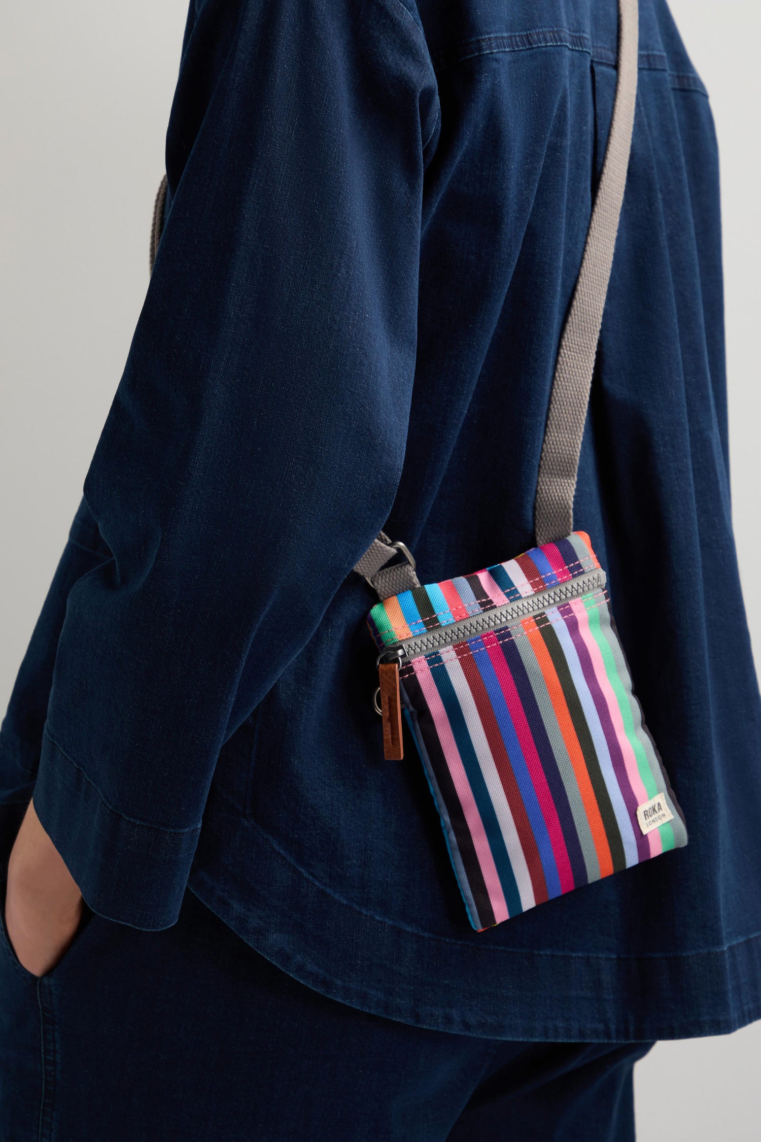 A person in a blue outfit stylishly carries a colorful striped Recycled Chelsea Crossbody Bag made from recycled material over their shoulder.