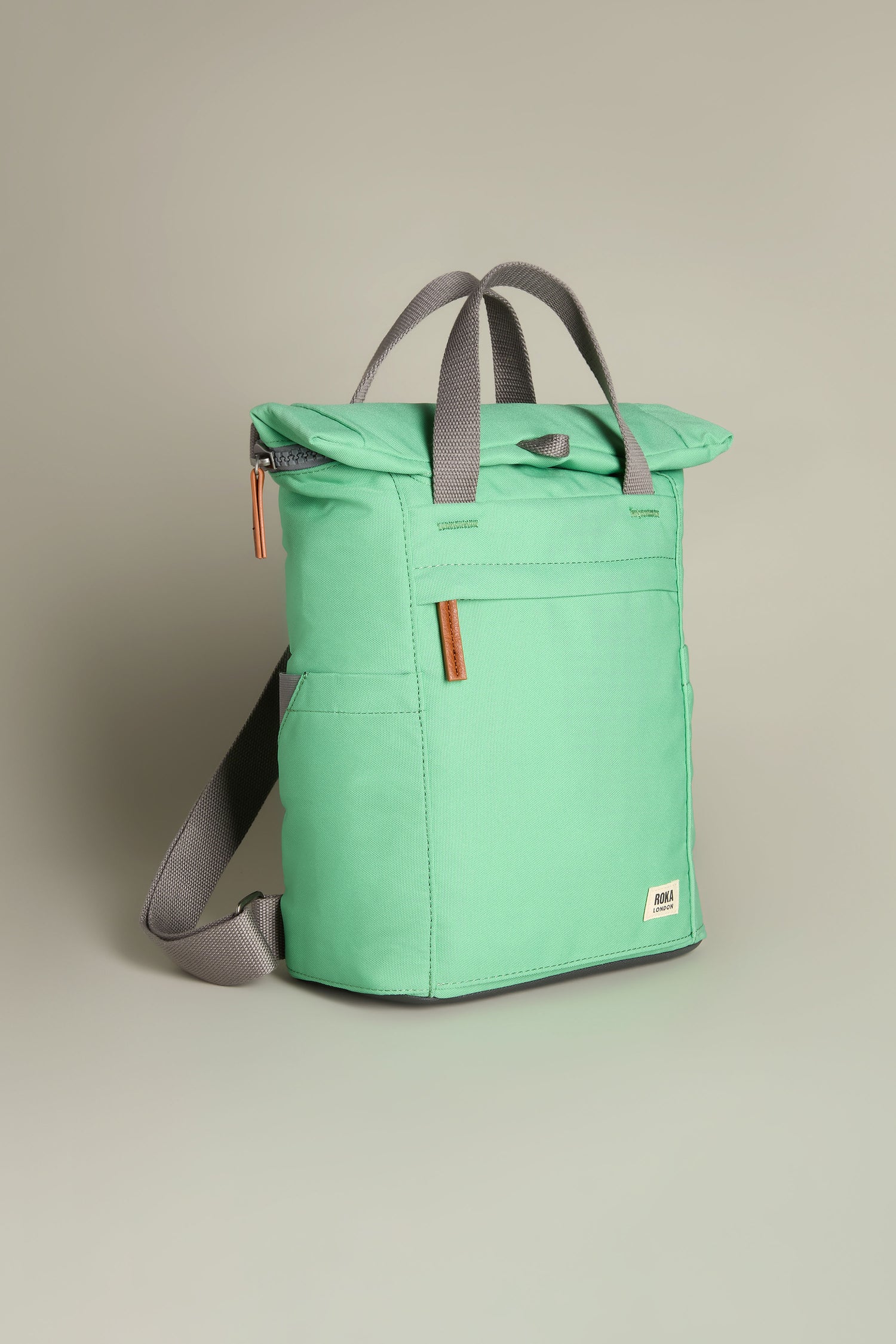 The Recycled Canvas Small Finchley Bag combines eco-conscious design with style, featuring gray handles and straps, a front pocket, and a secure zipper closure on a plain background.