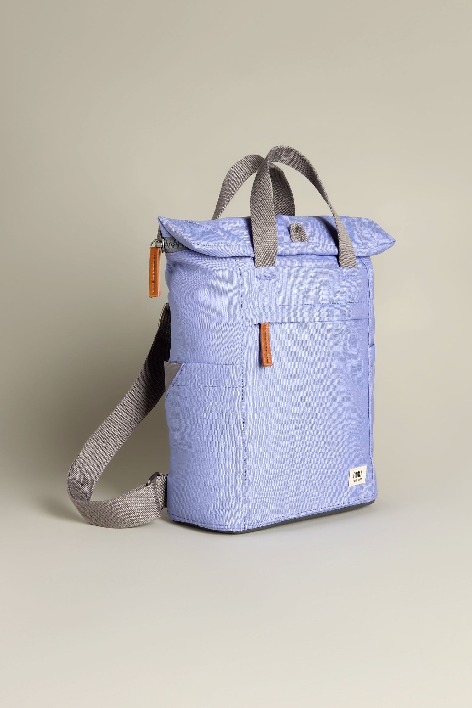 The Recycled Canvas Small Finchley Bag is a light purple backpack with gray handles and adjustable straps, brown zipper pulls, and a front pocket, offering an ideal sustainable option for eco-conscious travelers.