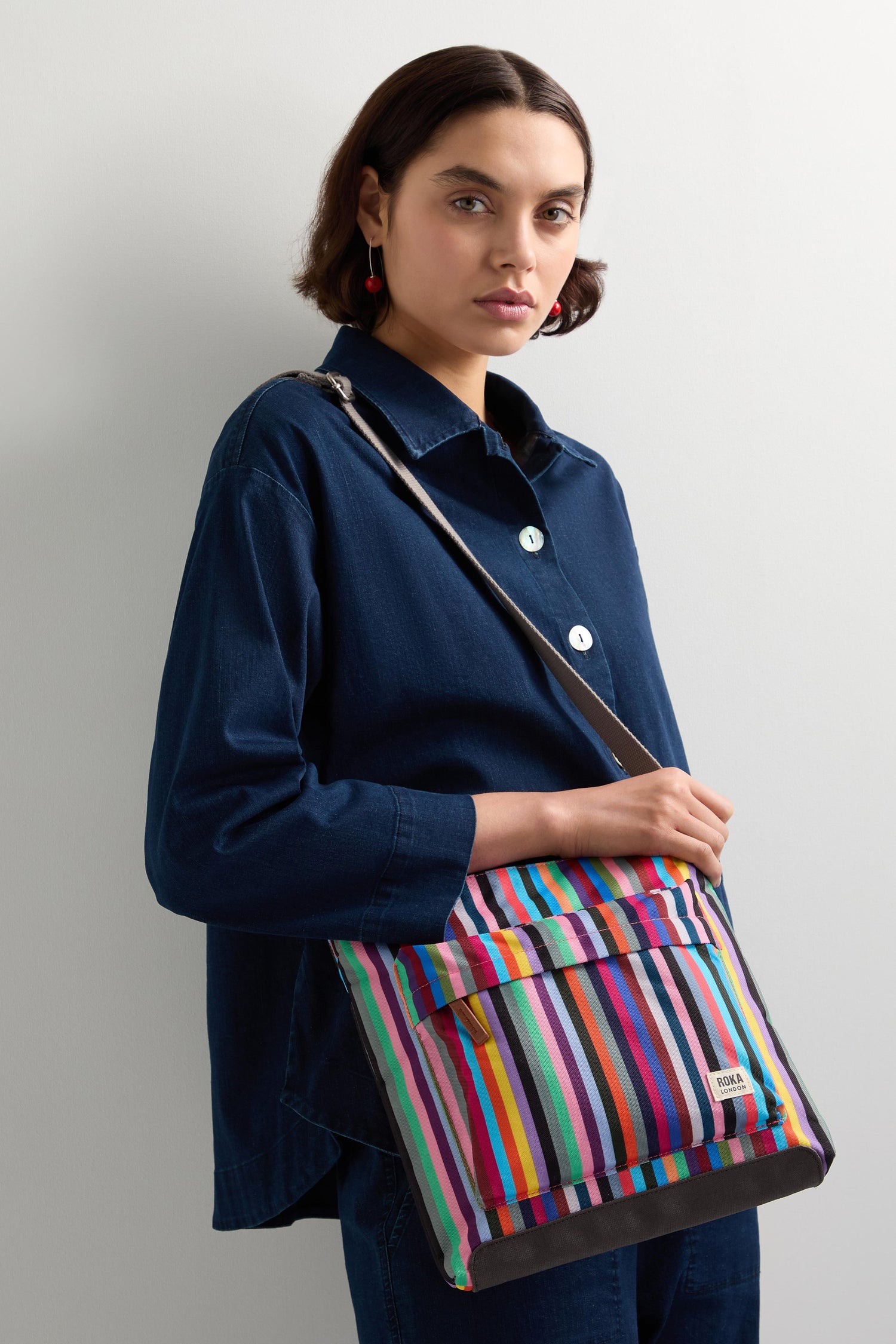 A person in a dark blue shirt holds an eye-catching Multi Stripe Recycled Canvas Kennington Bag, set against a plain background.