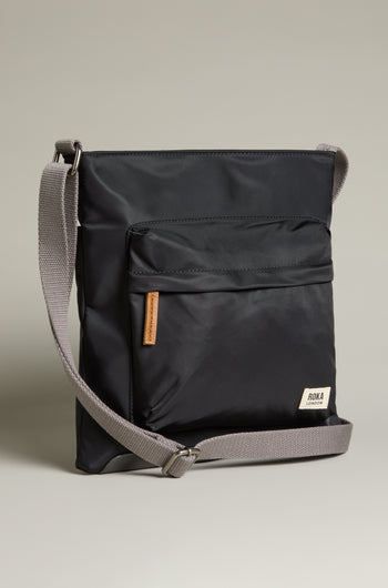 The Recycled Nylon Kennington Crossbody Bag is a sleek black accessory made from water-resistant fabric, featuring a gray adjustable strap and front pocket, set against a neutral background.