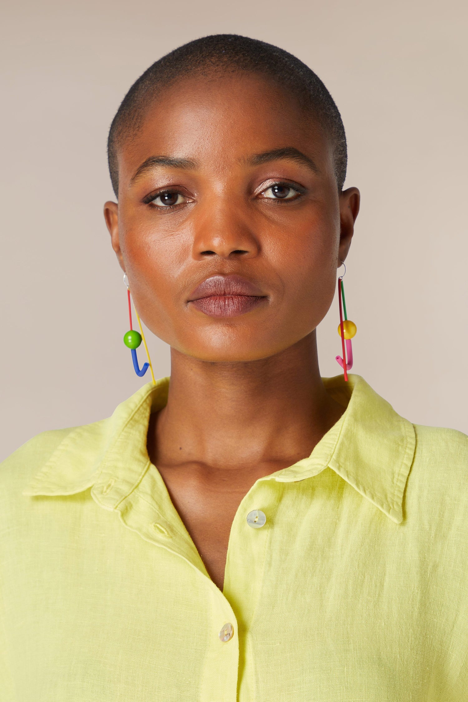 Portrait of a woman with a buzz cut wearing the Rainbow Sphere Earrings and a yellow shirt, looking directly at the camera.