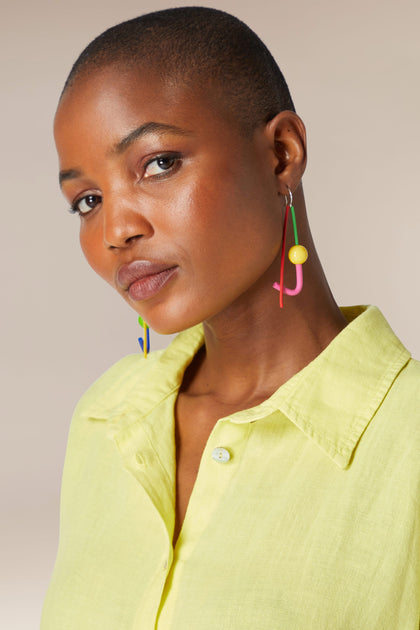 A woman with a buzz cut wearing Rainbow Sphere Earrings and a light yellow shirt, looking at the camera with a subtle smile.